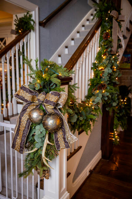 Decorative Christmas garland with gold ornaments and a bow on a staircase.