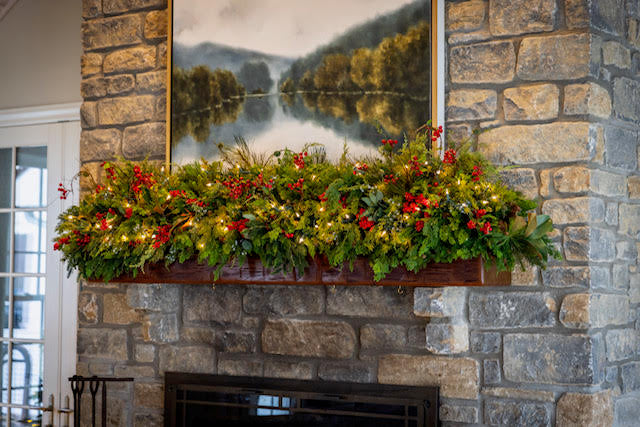 Decorative Christmas mantel with greenery and red berries on a stone fireplace.