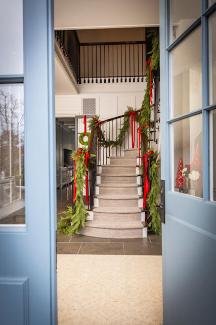 Decorative staircase with greenery and red ribbons inside a house, viewed through a blue door.