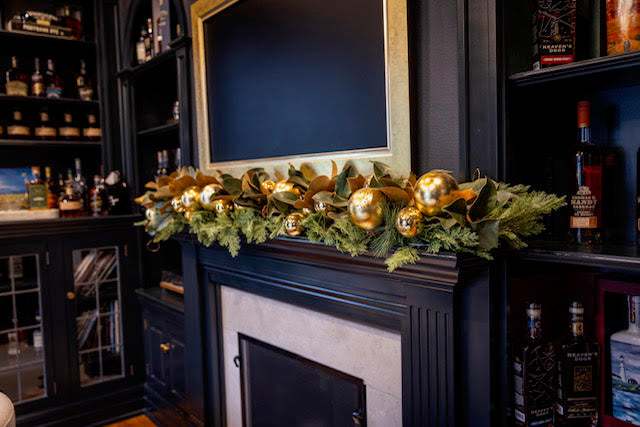 Decorative garland with gold balls on a fireplace mantel in a bar setting.