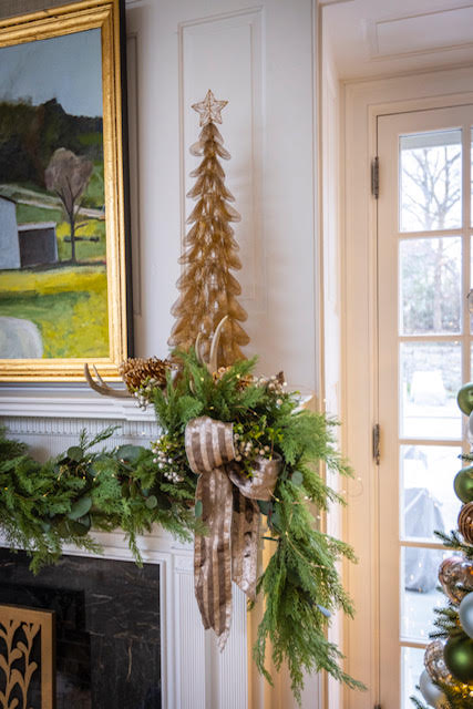 Decorative Christmas tree with greenery and ribbons on a mantel, with a painting and door in the background.