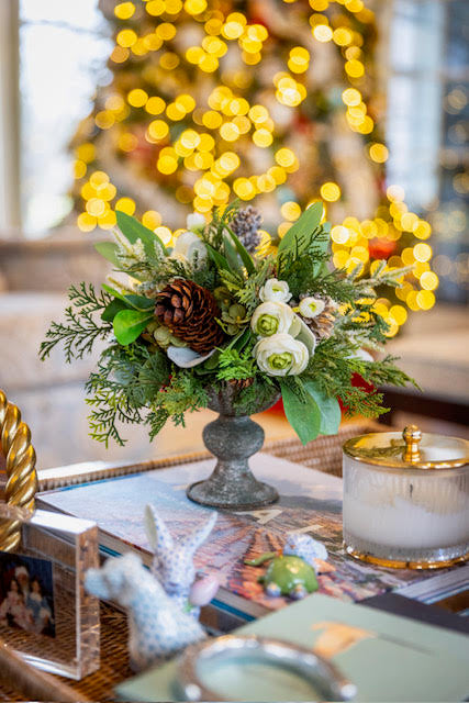 Decorative table setting with a floral arrangement, candles, and books against a blurred festive background.
